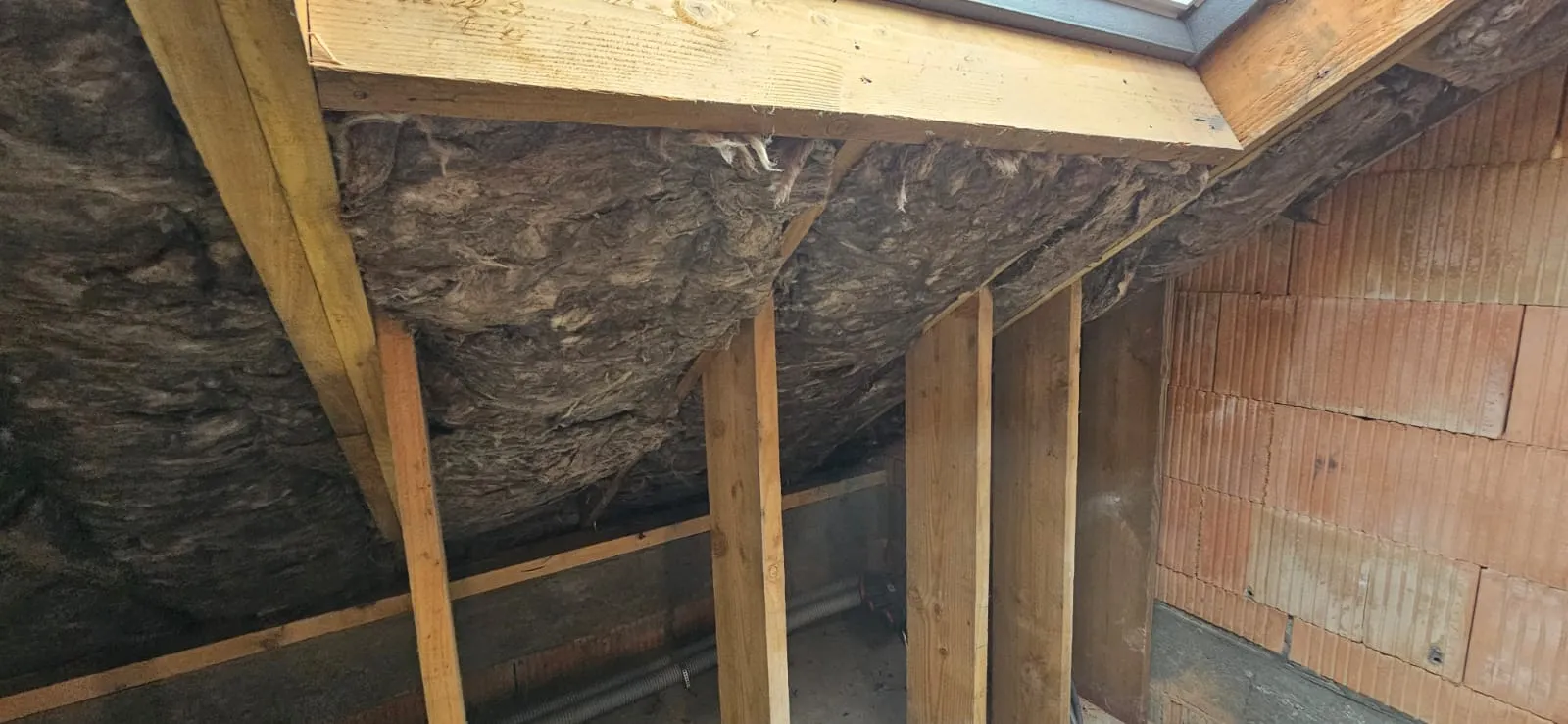 Combles avant isolation — chevrons en bois apparent et laine minérale entre les rampants