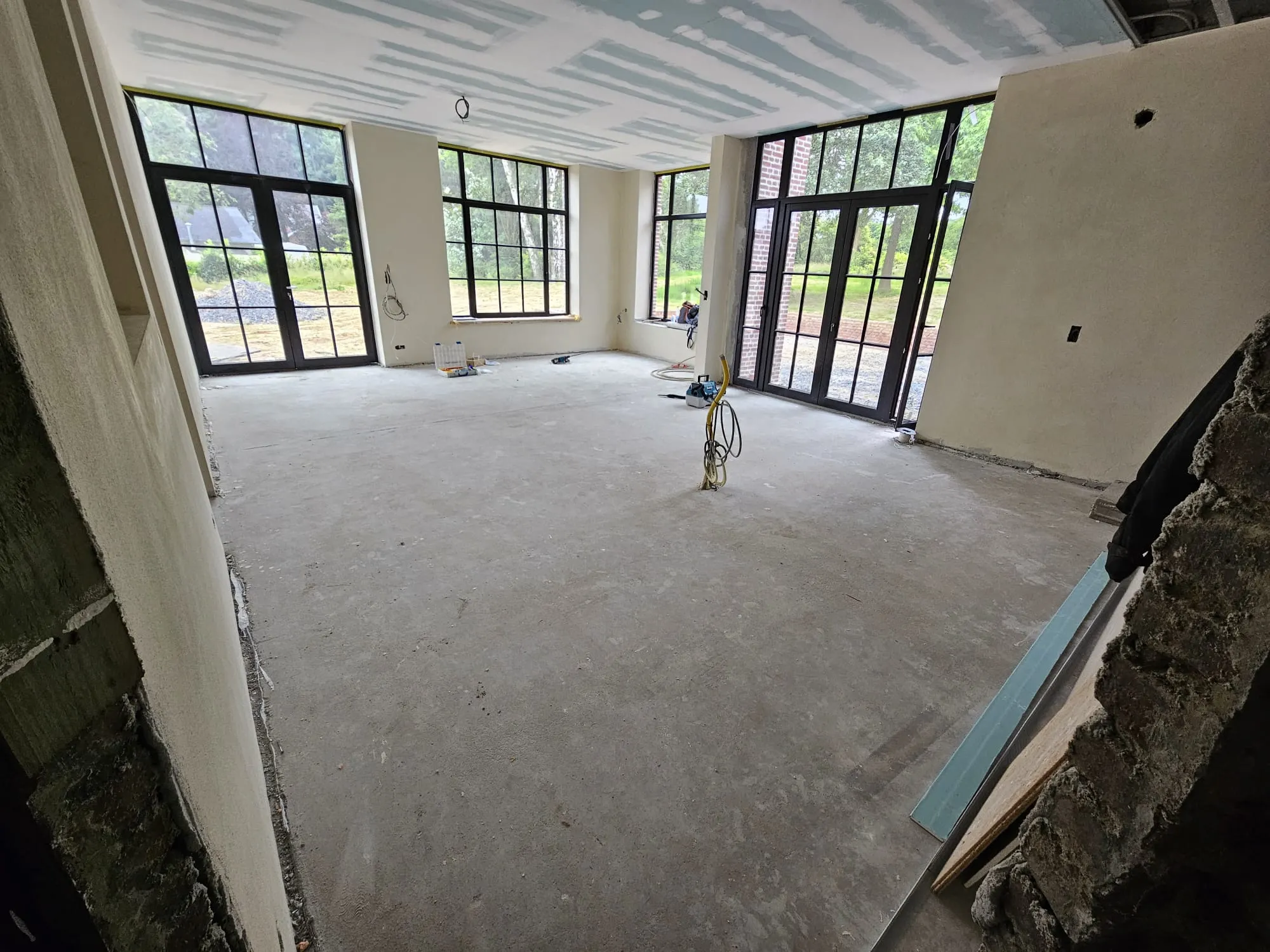 Loft contemporain avec trois grandes baies en acier laissant entrer la lumière, sols en béton brut